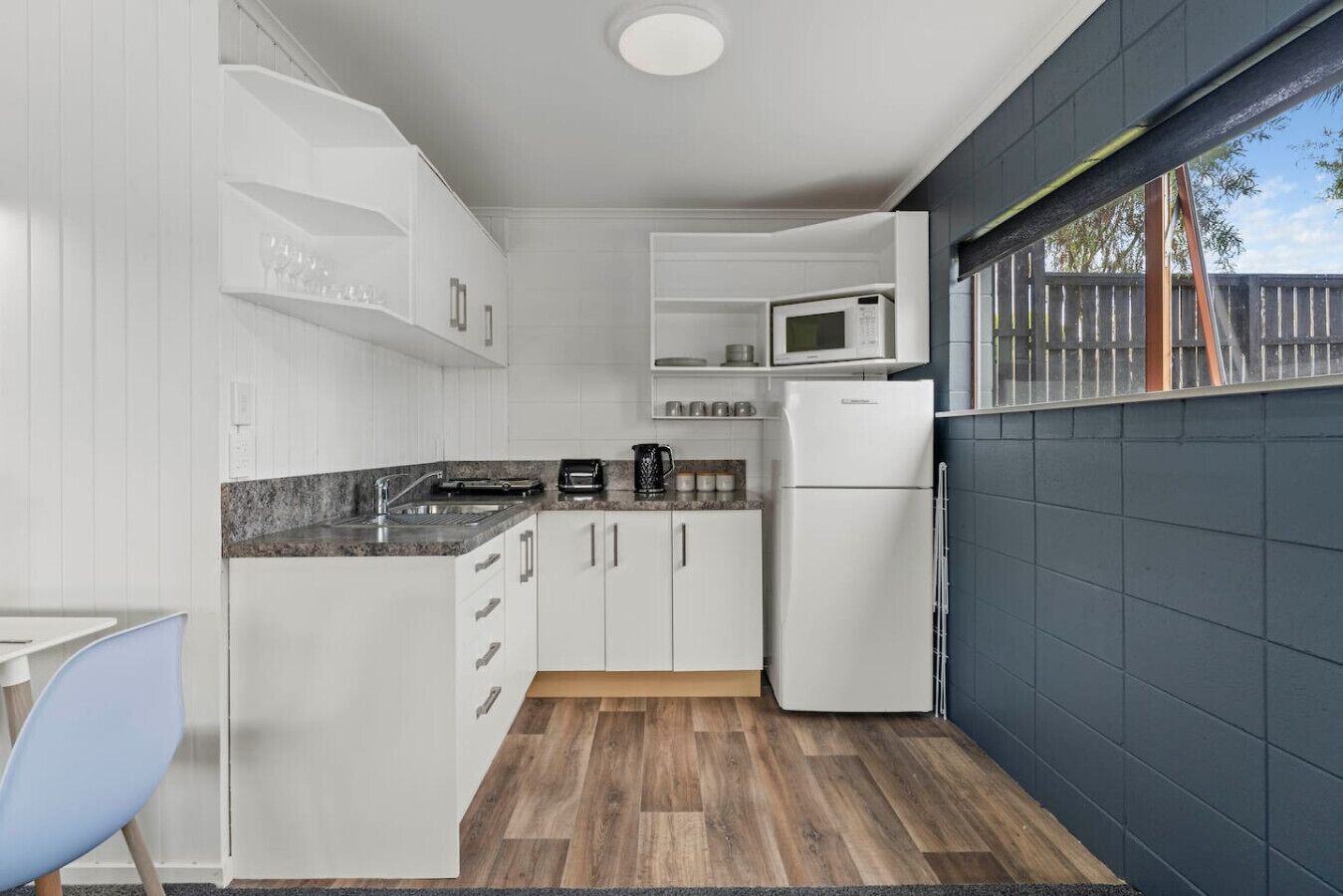 A compact kitchen with white cabinets, a microwave, a toaster, and a refrigerator.
