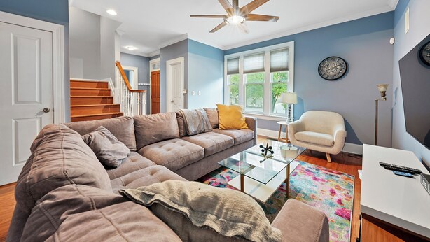 A living room with a sectional sofa, a glass coffee table, a white armchair, and a ceiling fan. - Combined 2 homes-9BR/8 BTH, 25 beds Best Location. Perfect for Large Groups (Columbus)