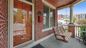 A brick building with a wooden door, a porch with a swing bench, and a mailbox. - Combined 2 homes-9BR/8 BTH, 25 beds Best Location. Perfect for Large Groups (Columbus)