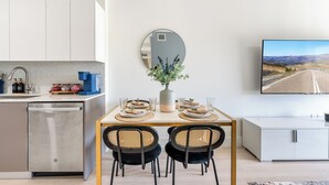 Une cuisine moderne équipée d’un lave-vaisselle, d’une table à manger avec deux chaises, d’un vase agrémenté de plantes et d’un téléviseur à écran plat fixé au mur.
