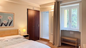 A hotel room with a bed, bedside table with a lamp, a door, a bench, and a window with curtains. - Colorful studio- Bramante 41 (Milan)