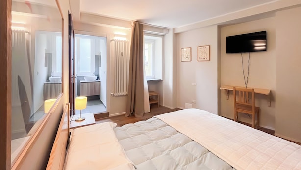 A hotel room with a bed, bedside lamp, TV, and a desk. - Colorful studio- Bramante 41 (Milan)