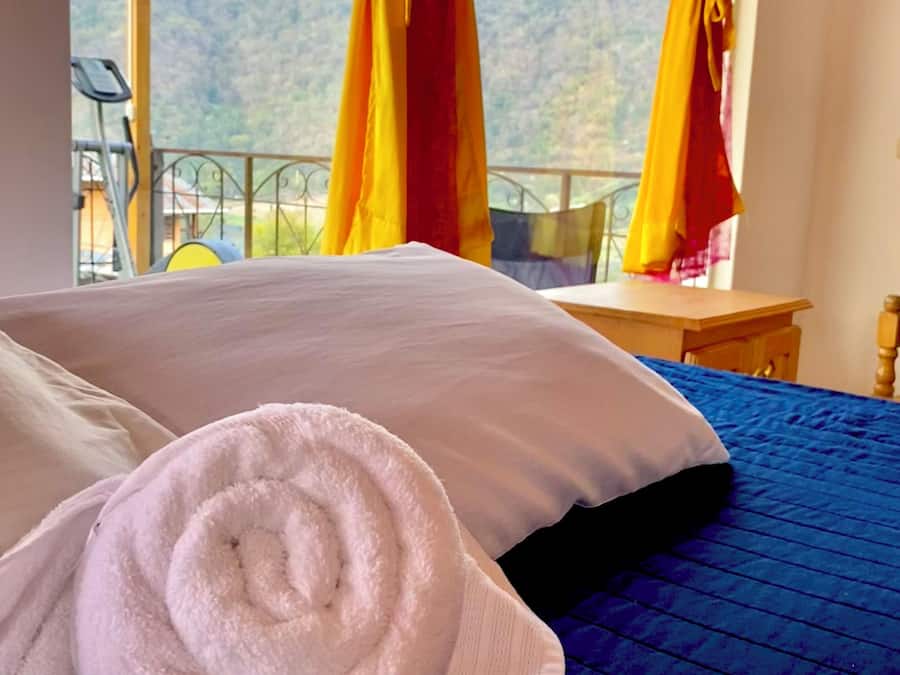 A bed with a blue quilt and white pillows, a rolled white towel, and yellow curtains.