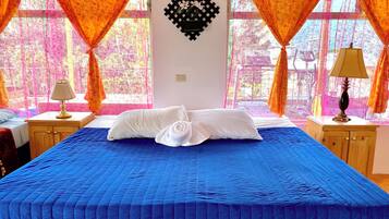 A hotel room with a large bed, two bedside tables, a wall-mounted decorative item, and large windows with curtains.
