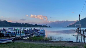 A calm lake with boats docked at a pier, surrounded by hills. - Hotel Minnesota (San Lucas Tolimán)