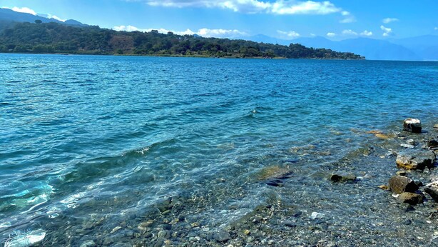 A clear view of a lake with rocky shoreline and distant hills. - Hotel Minnesota (San Lucas Tolimán)