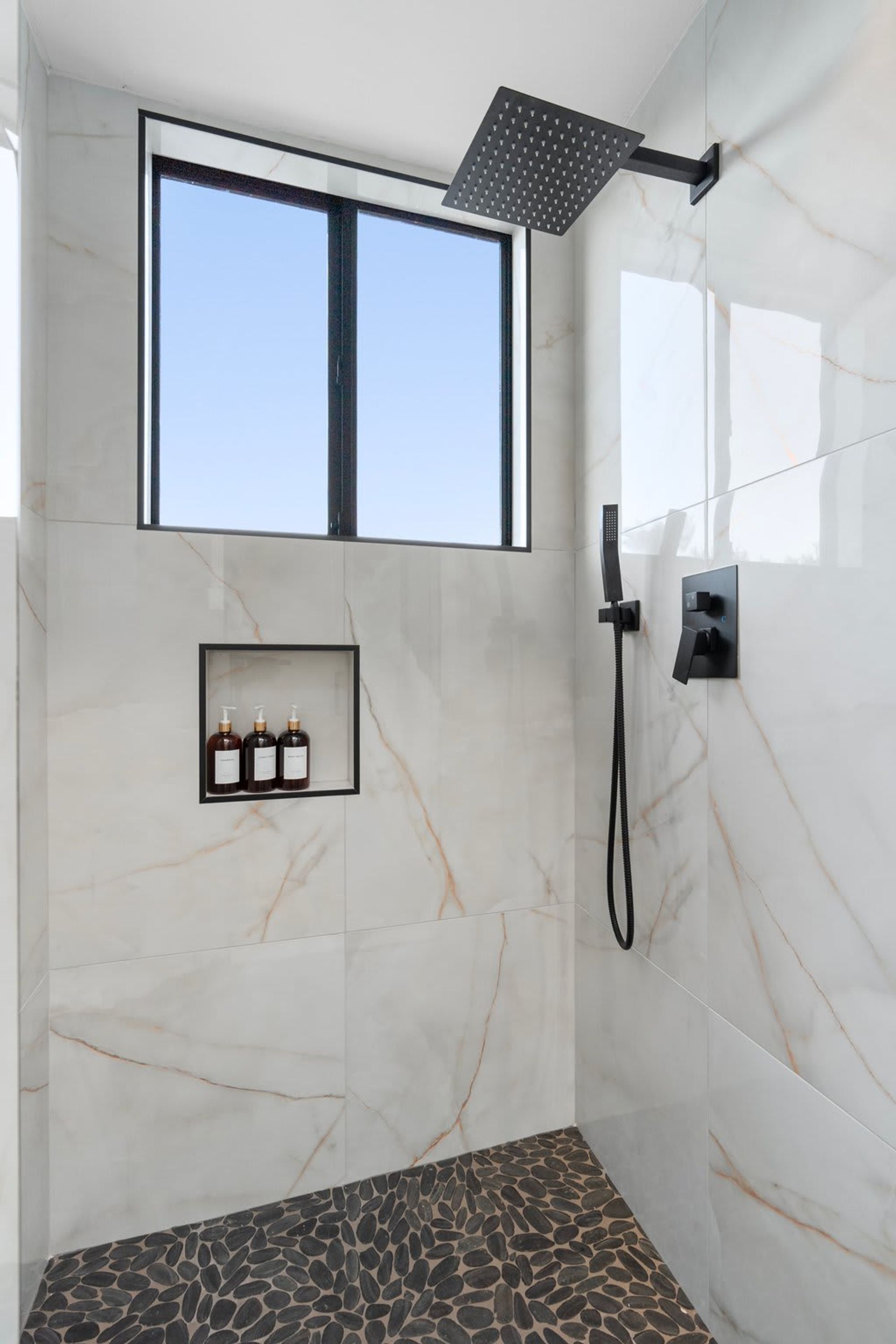 A modern bathroom with a shower, a window, and a shelf with toiletries.
