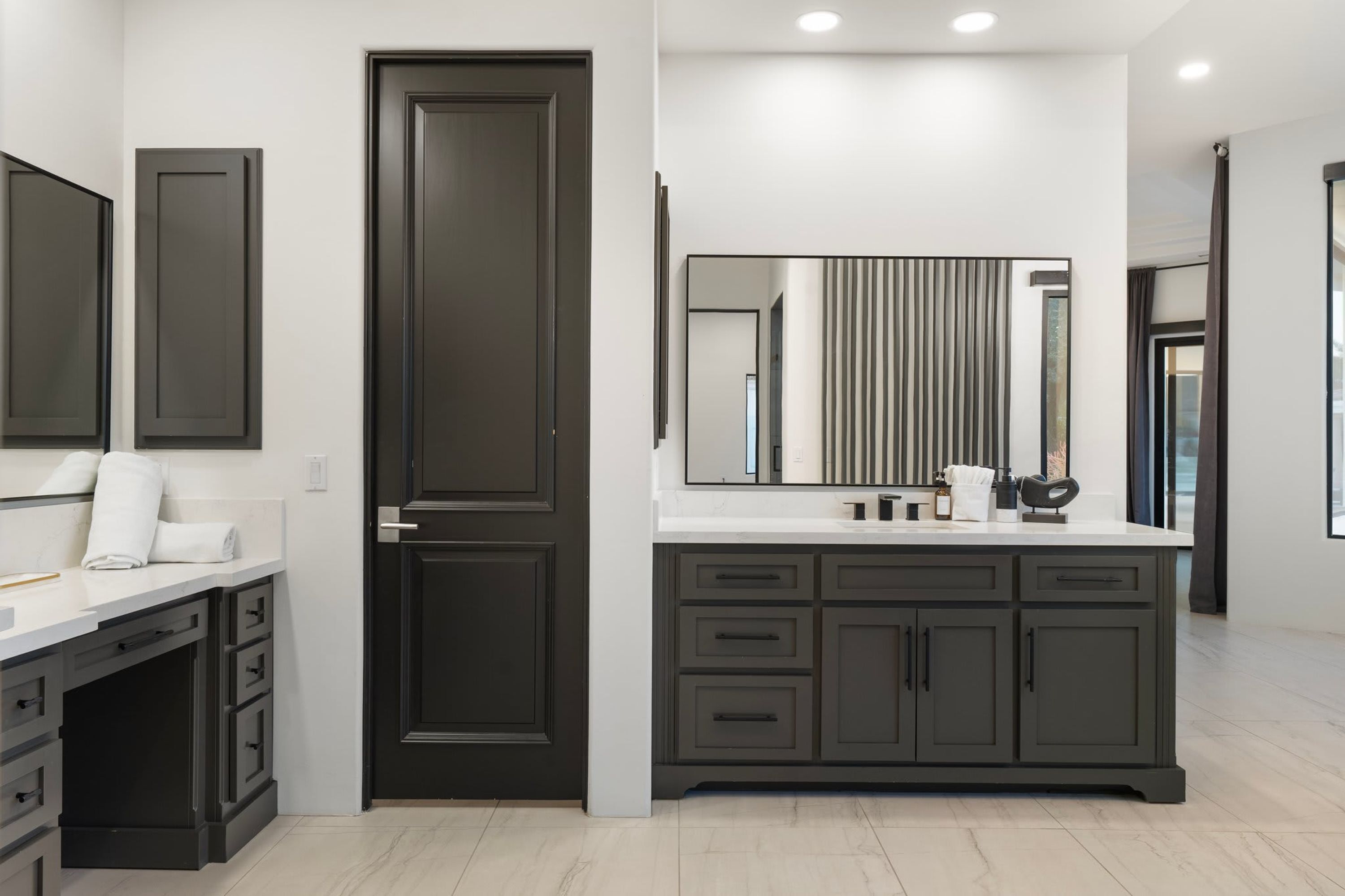 A modern bathroom with a dark door, a large mirror, and a white countertop.