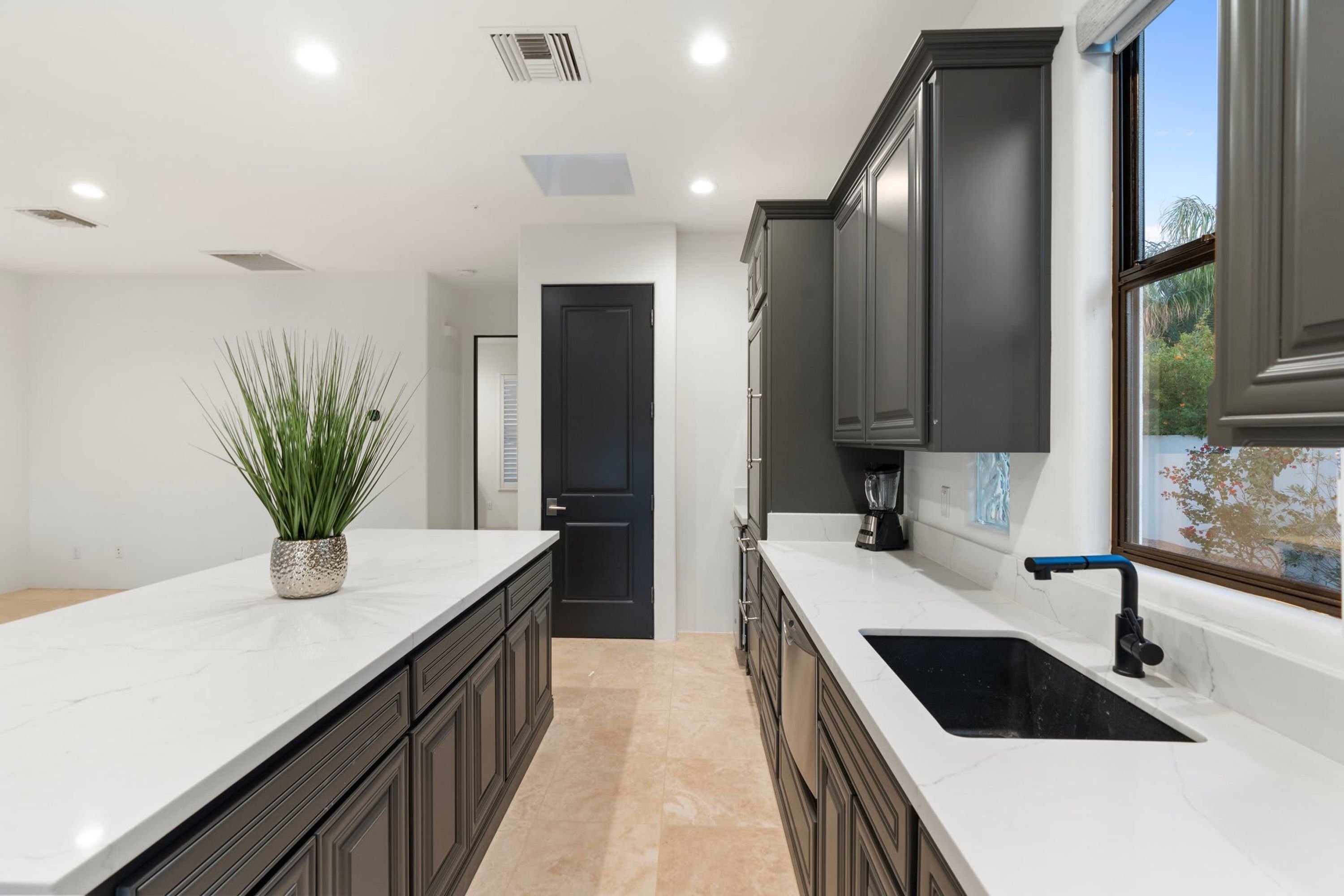 A modern kitchen with dark cabinets, a white countertop, and a black sink.
