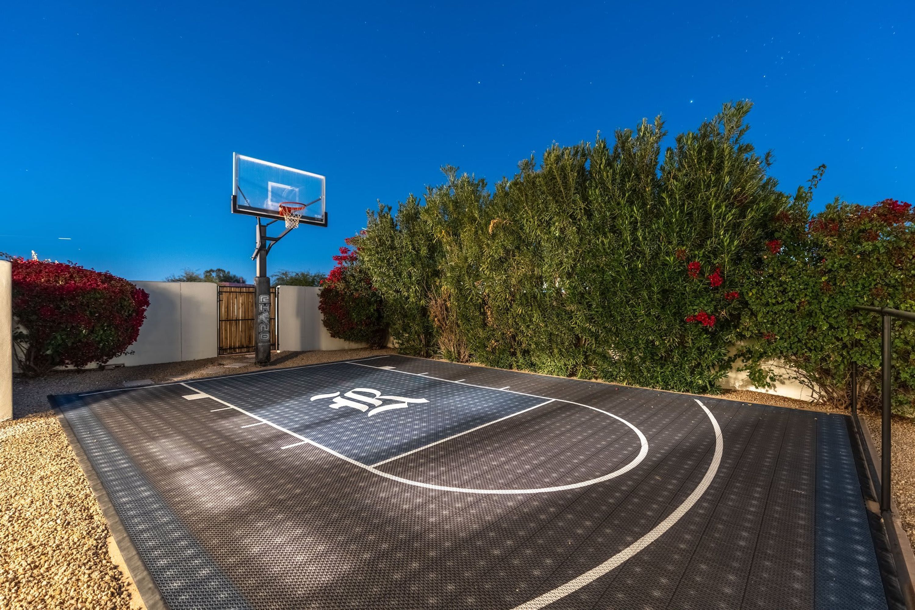 Een basketbalveld met een ring, omgeven door groen en een heldere lucht.