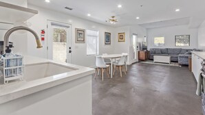 A modern kitchen with a large island, white walls, and a dining area with a gray sofa and white chairs. - Historic Garfield Industrial 1 BR Minutes to DT PHX (Phoenix)