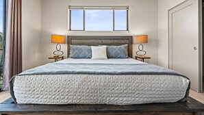 A large bed with a quilted mattress, two bedside lamps, a window above the bed, and a door to the right. - Moondance Redrock Terrace Sedona (Sedona)
