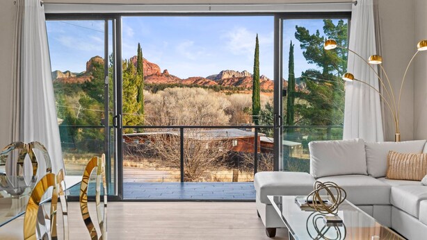 A spacious living room with a glass coffee table, a white sofa, and a view of red rock formations through large sliding glass doors. - Moondance Redrock Terrace Sedona (Sedona)