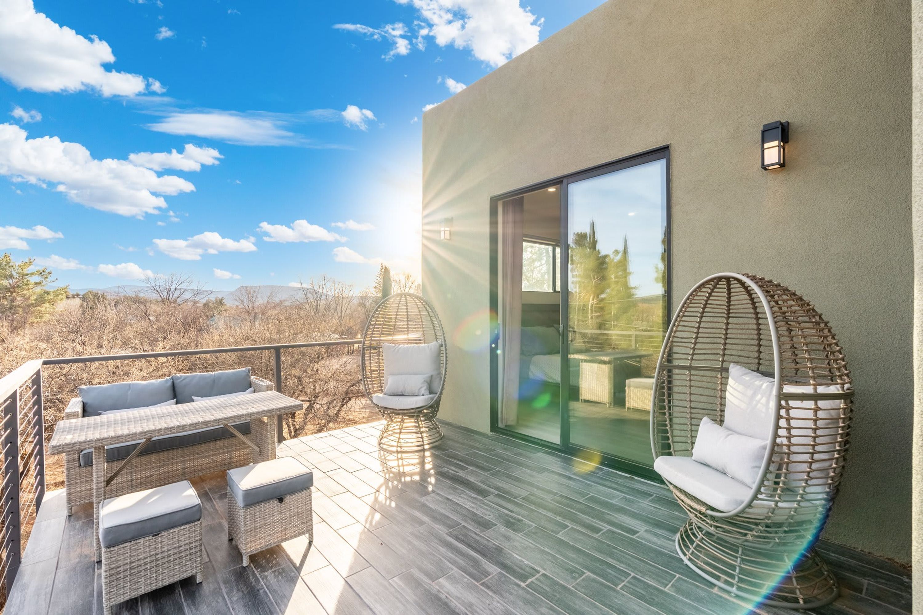 A modern outdoor deck with wicker furniture and a glass door leading to a room.