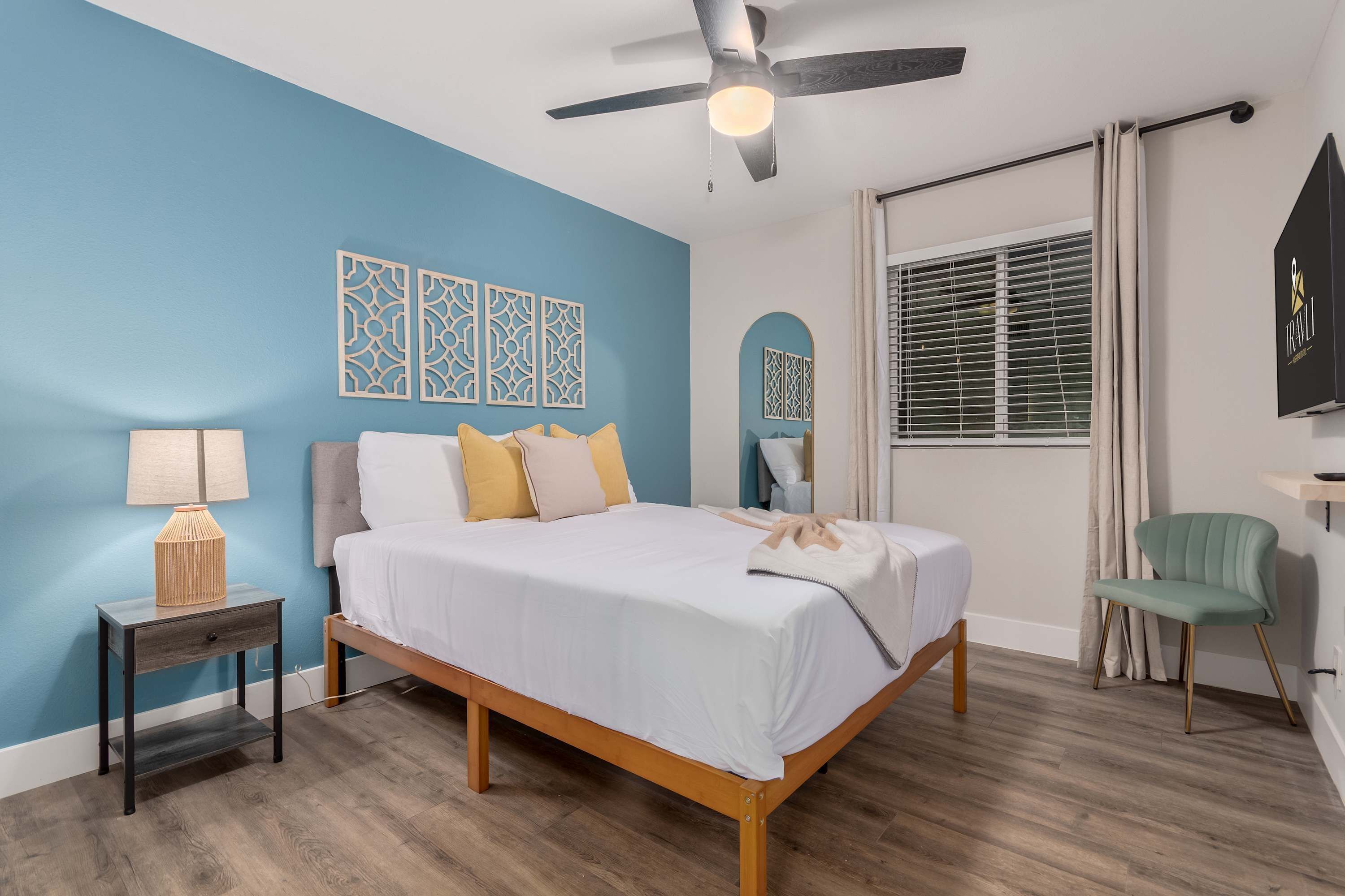 A bedroom with a bed, a nightstand, a chair, a ceiling fan, and decorative wall panels.