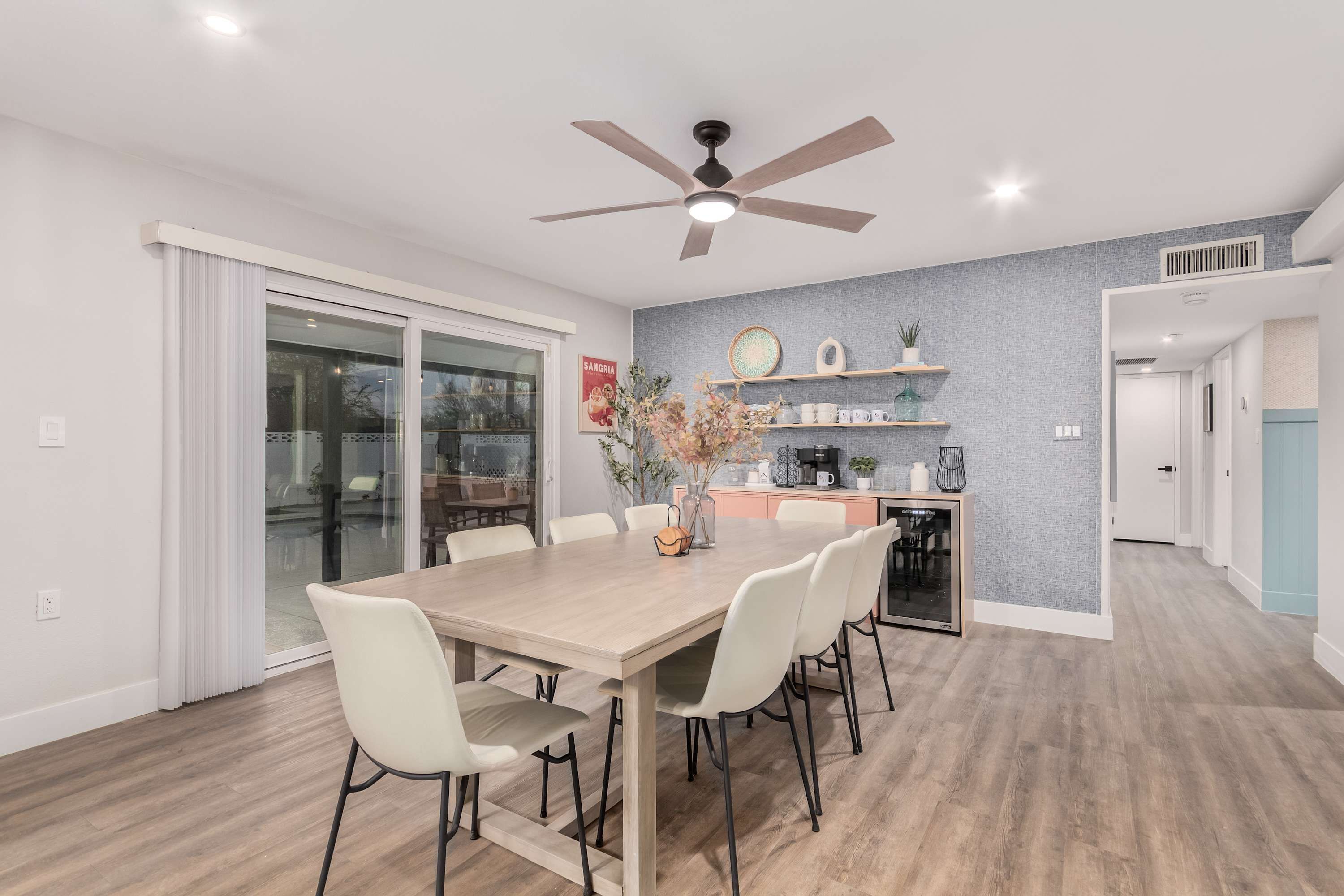 A modern dining area with a wooden table, white chairs, and a ceiling fan.