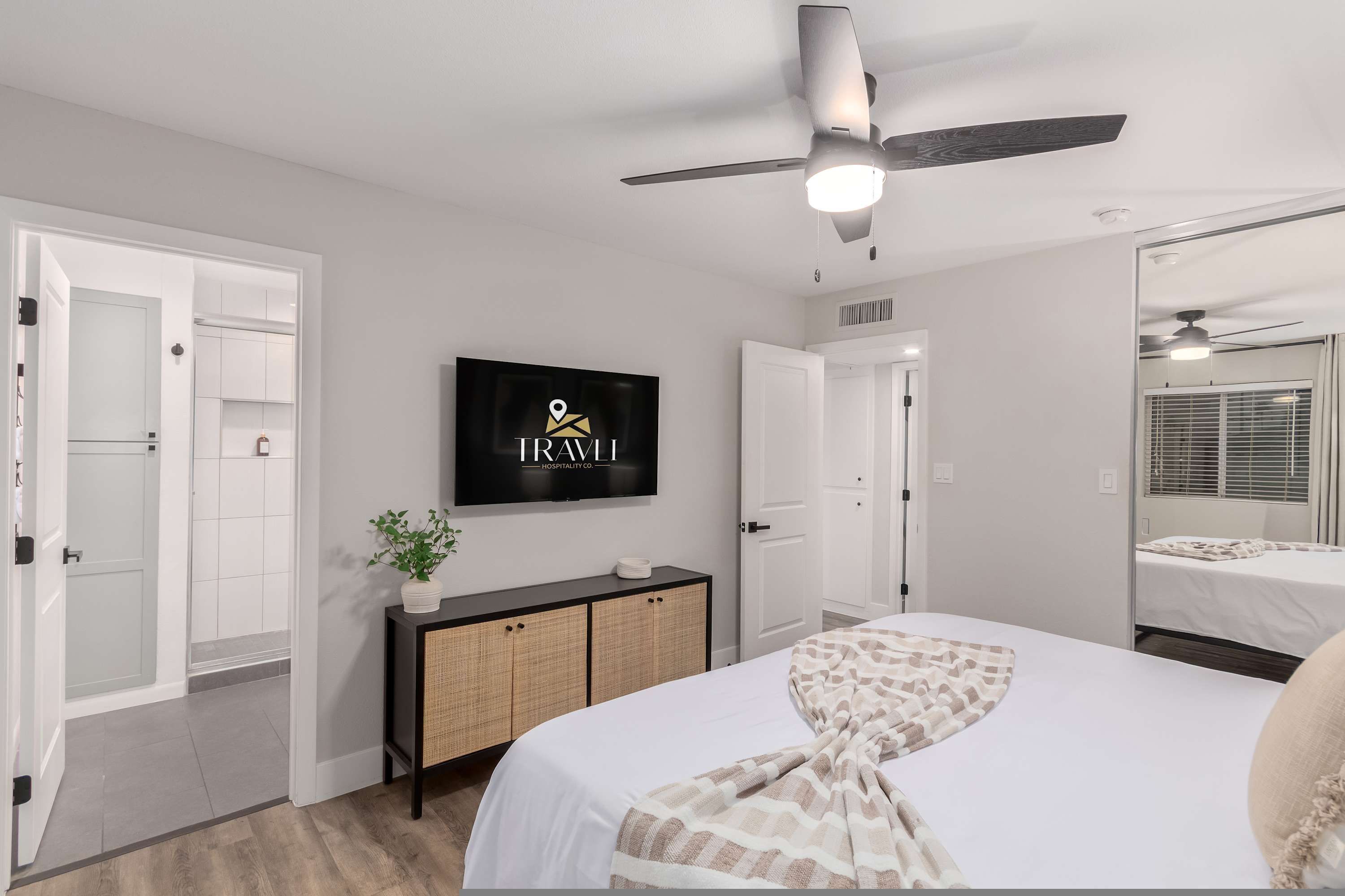 Una habitación de hotel con una cama, un televisor en la pared, un ventilador de techo y una puerta que da a un baño.