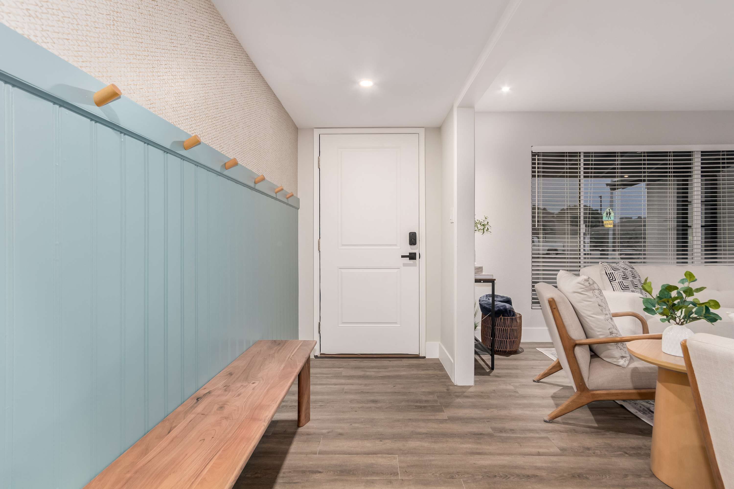 A hallway with a wooden bench, a white door, and a seating area with a sofa and a table.