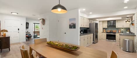 Una cocina moderna con armarios blancos, una mesa de comedor de madera y una lámpara colgante.