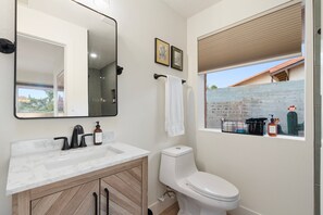 A bathroom with a white toilet, a sink with a marble countertop, and a large mirror. There is a window with a view of a brick wall and a cactus. - NEW Redrock Experience Views Firepit Hottub (Sedona)
