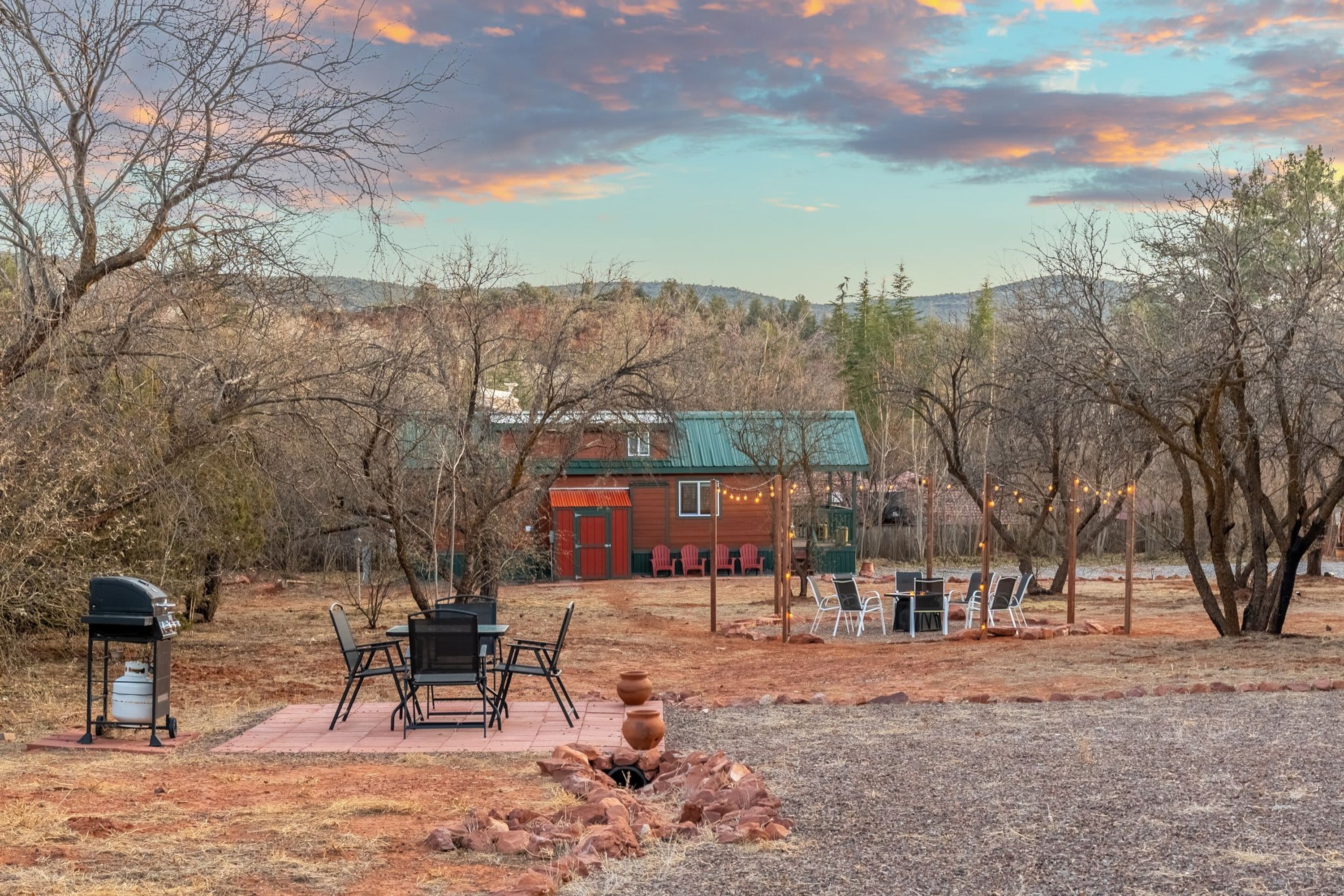 A rustic cabin with a red door, surrounded by a patio with outdoor furniture, a grill, and a decorative fire pit.
