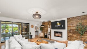 Un salon moderne avec un canapé blanc, une table basse et une cheminée. Une grande fenêtre offre une vue sur l’extérieur.