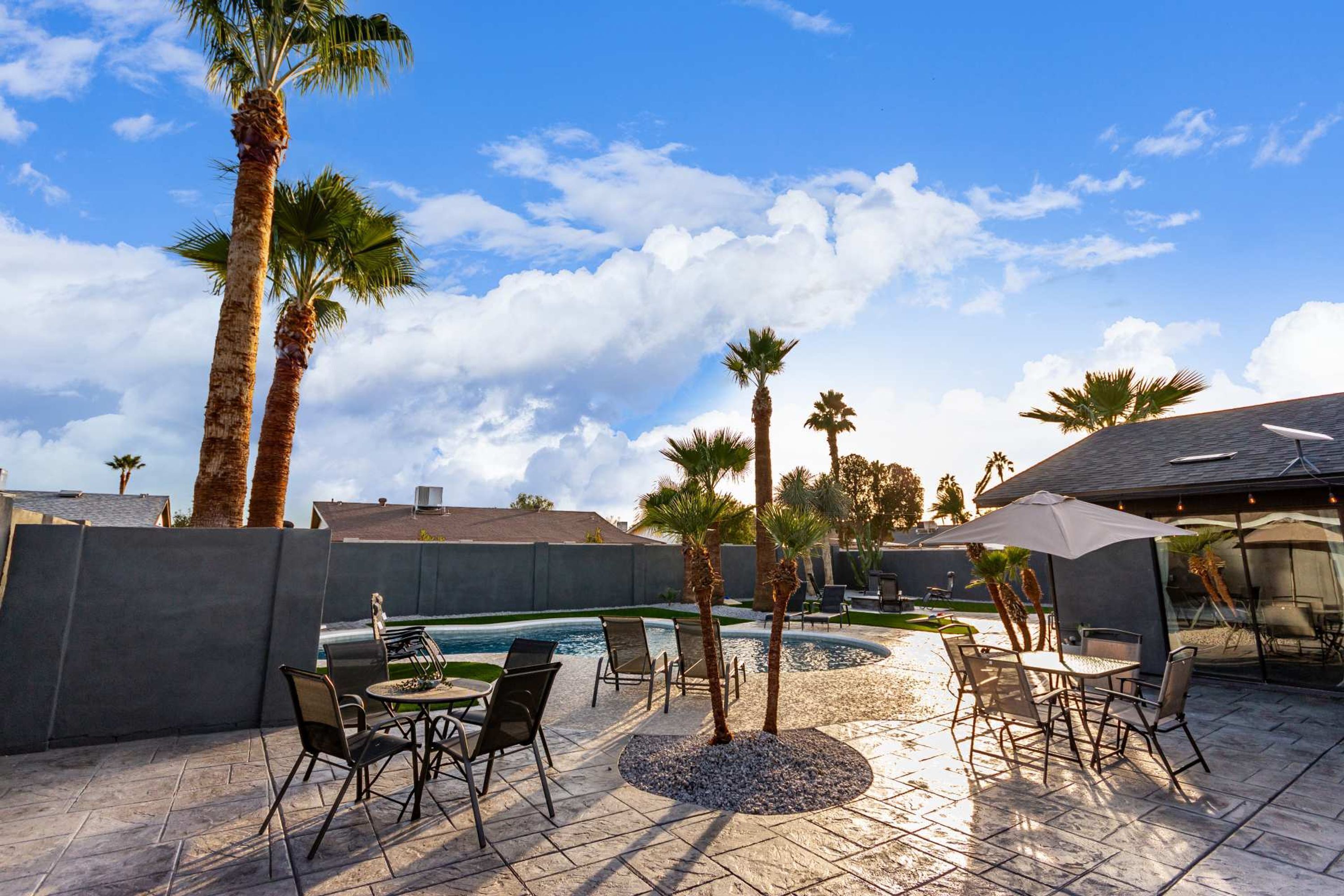 Eine Terrasse im Freien mit Pool, Palmen und Gartenmöbeln.