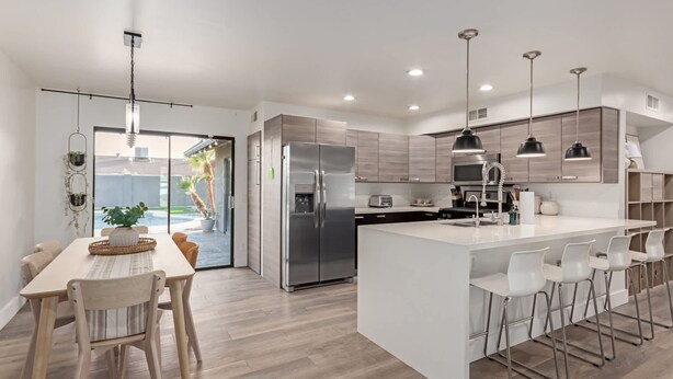 Une cuisine moderne dotée d’un îlot central, d’appareils électroménagers en acier inoxydable, de luminaires suspendus et offrant une vue sur l’extérieur.