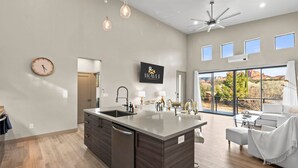 A modern kitchen with a central island, a dining area with a white sofa, and large windows offering a view of the outdoors. - NEW Moondance Red Rock Retreat Epic Views (Sedona)