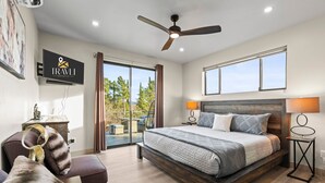 A modern hotel room with a large bed, a ceiling fan, a TV displaying the hotel name, a balcony with outdoor furniture, and a view of trees. - NEW Moondance Red Rock Retreat Epic Views (Sedona)