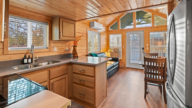 A cabin interior with wooden walls, a kitchen with a sink and stove, a dining area with a table and chairs, and a large refrigerator. - NEW Moondance Majestic Mini Cabin Cathedral Rock (Sedona)