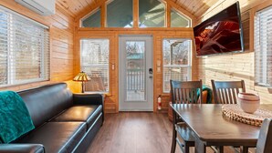 A cozy cabin interior with a wooden ceiling, a black leather couch, a dining table with chairs, and a mounted TV. - NEW Moondance Majestic Mini Cabin Cathedral Rock (Sedona)