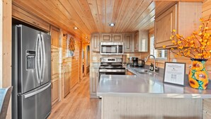 A modern kitchen with stainless steel appliances, wooden cabinetry, and a central island. - NEW Moondance Majestic Mini Cabin Cathedral Rock (Sedona)