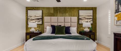 A modern hotel bedroom with a large bed, a ceiling fan, two nightstands with lamps, and artwork on the walls.