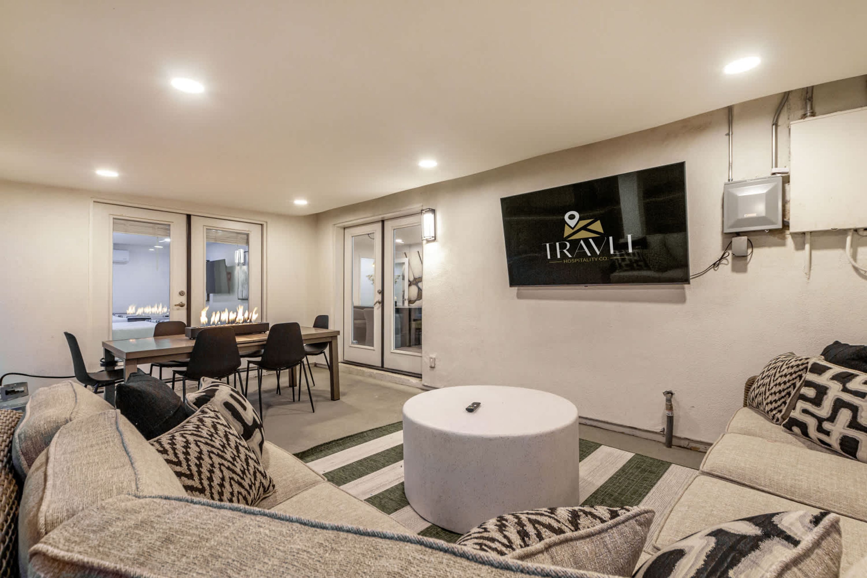 A modern living room with a sofa set, a round ottoman, and a dining area with chairs and a table.