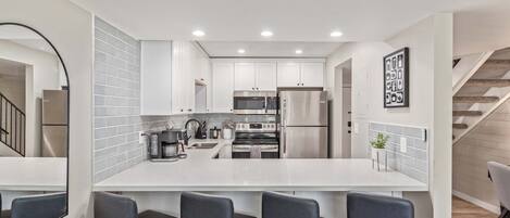 Una cocina moderna con armarios blancos, electrodomésticos de acero inoxidable y una isla central con taburetes de bar.