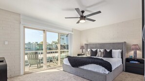 A bedroom with a large bed, a ceiling fan, a nightstand, and a view through a sliding glass door to an outdoor area. - New-heatherbrae 8-old Town-camelback View (Scottsdale)