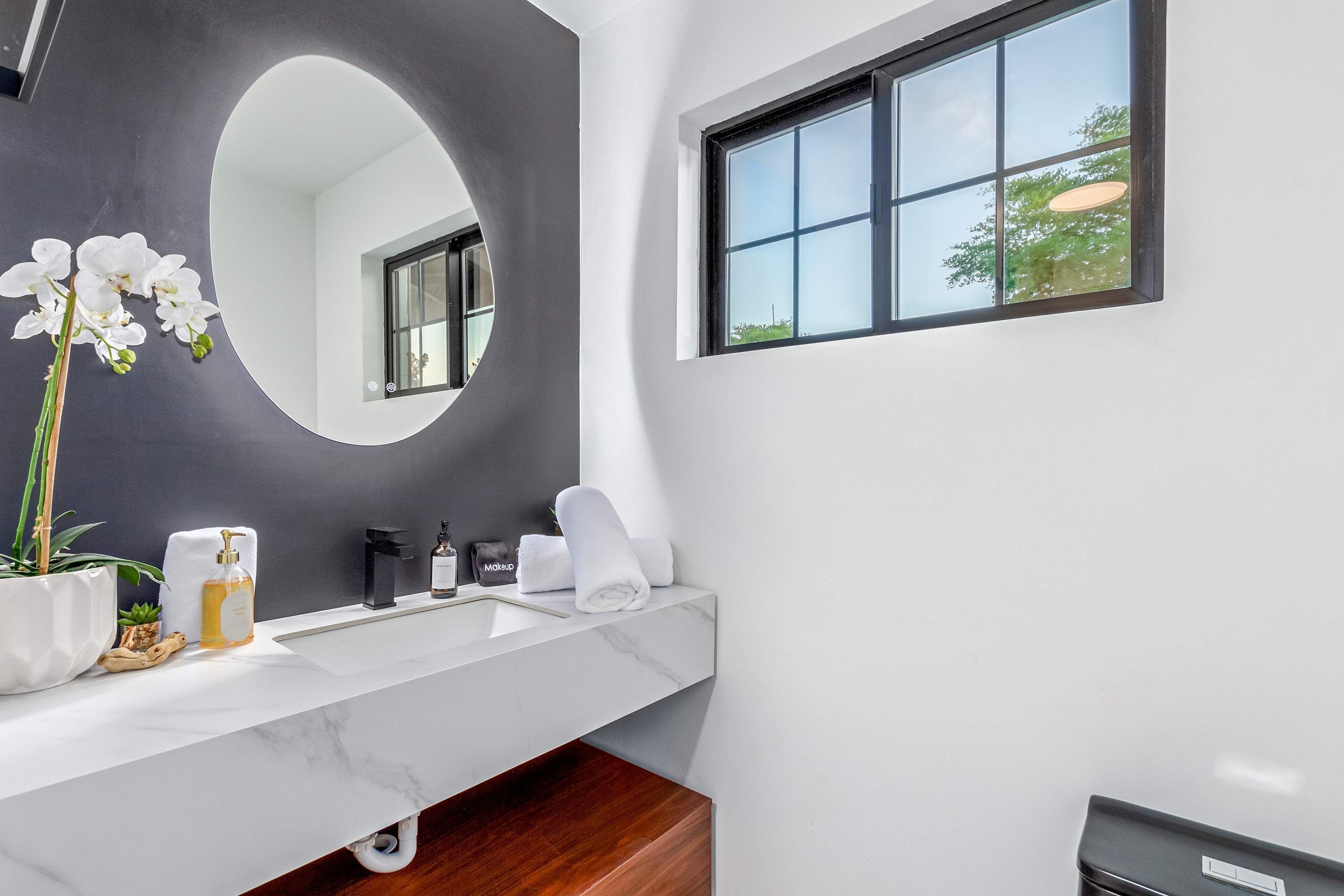 Une salle de bain moderne avec un lavabo en marbre blanc, un grand miroir, une fenêtre donnant sur un beau paysage et une orchidée en pot.