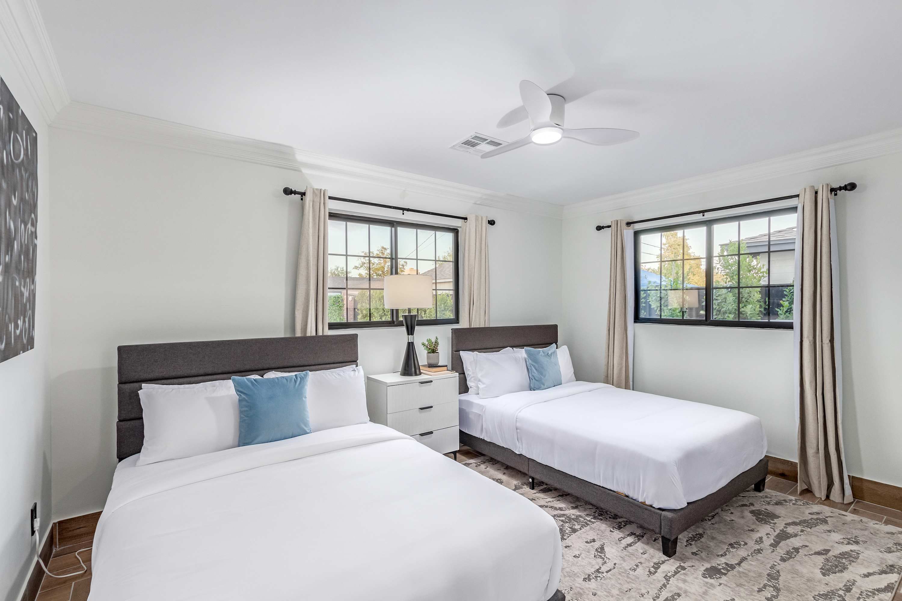 A hotel room with two beds, a ceiling fan, and large windows with curtains.