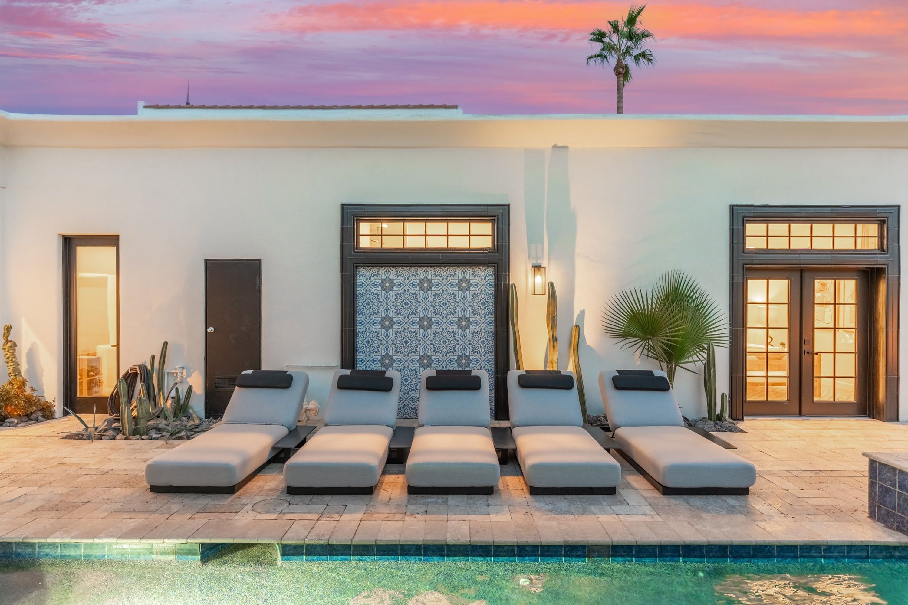A modern outdoor pool area with lounge chairs, a patterned wall, and a palm tree.