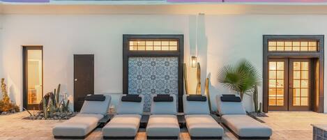 A modern outdoor pool area with lounge chairs, a patterned wall, and a palm tree.