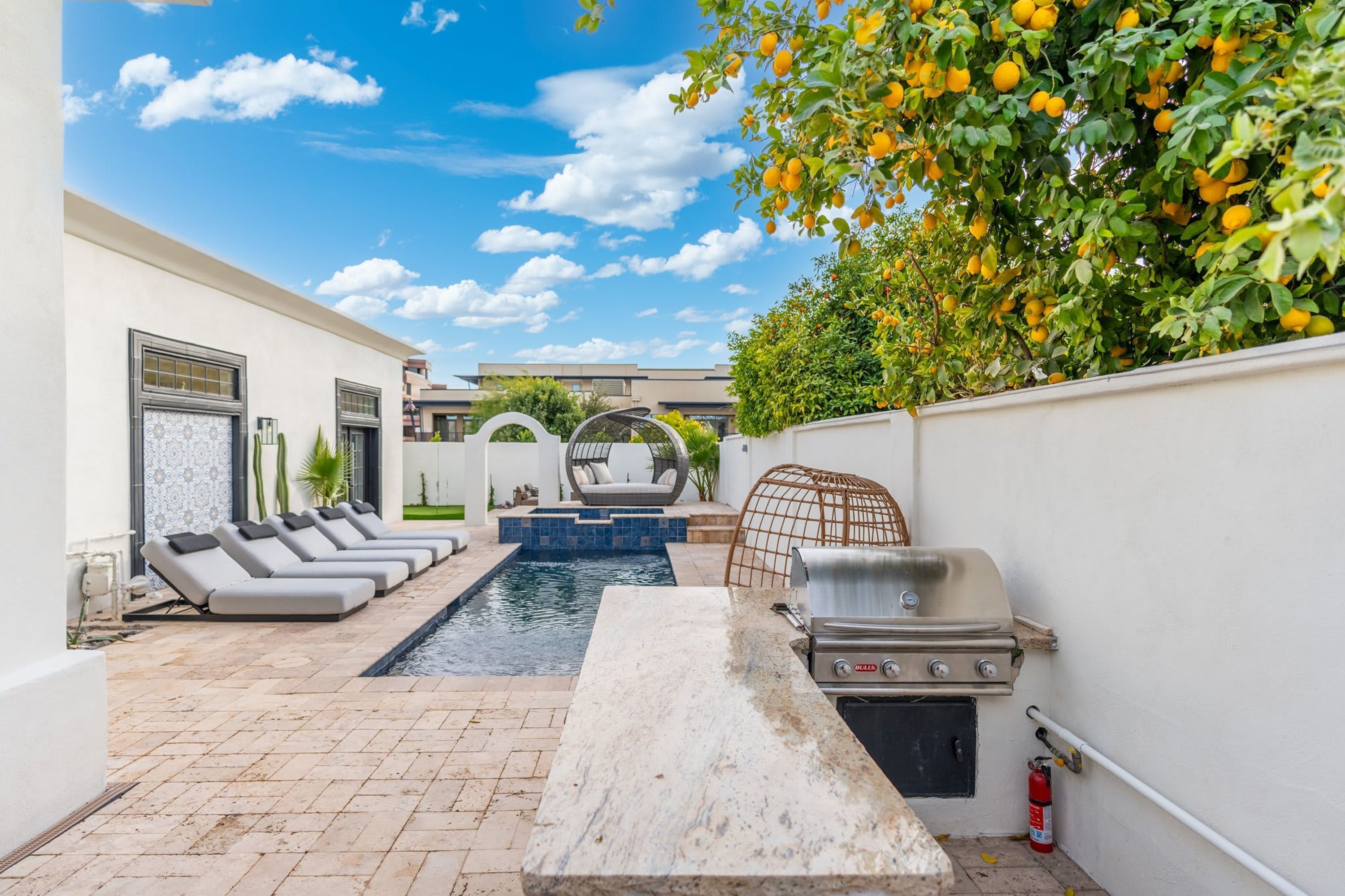 A pool area with lounge chairs, a barbecue grill, and a fire extinguisher.
