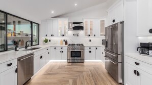 A modern kitchen with white cabinetry, stainless steel appliances, and a herringbone wood floor. - NEW The Kensington Custom Pool Al-fresco Living (Scottsdale)