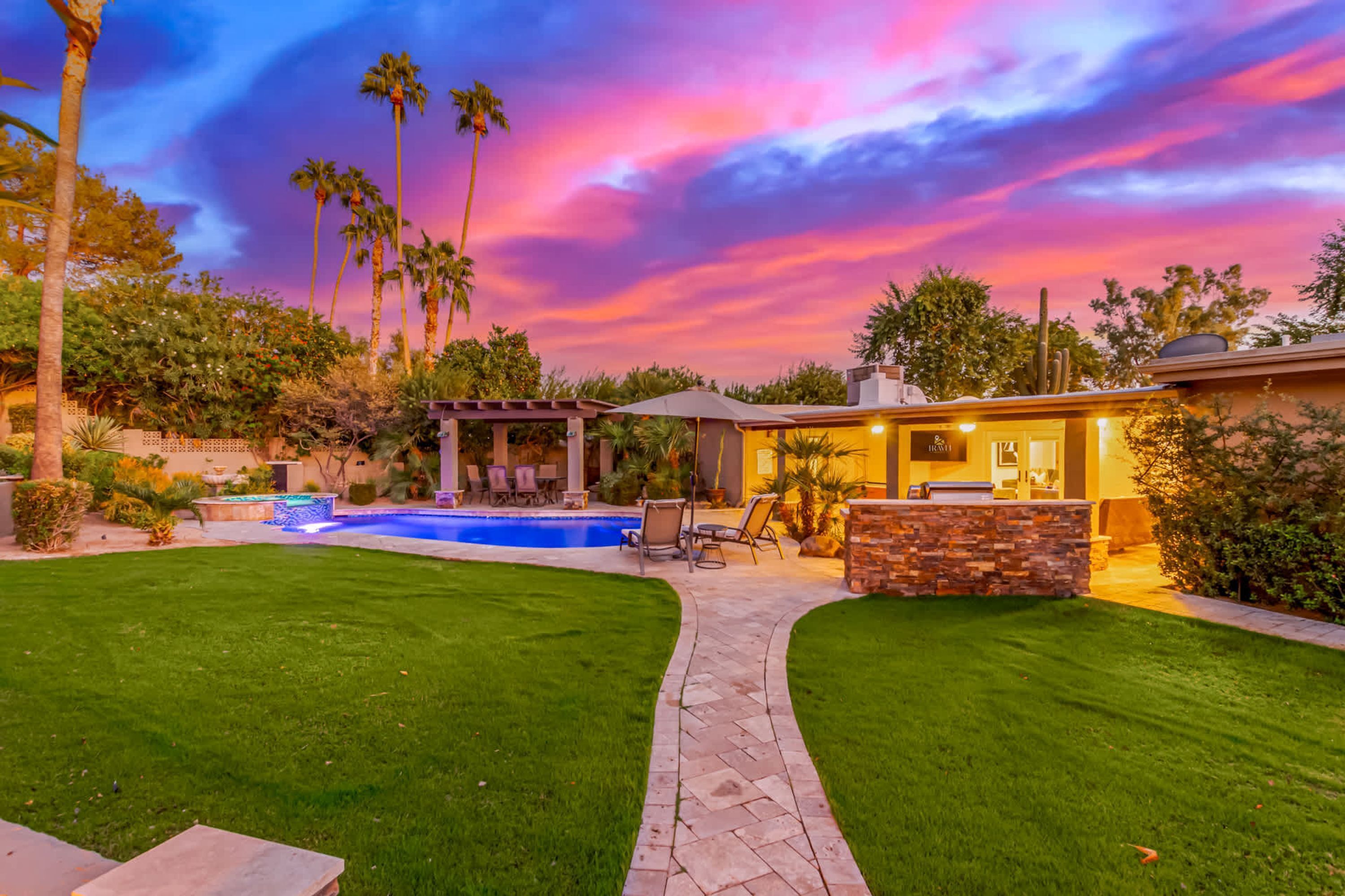 A backyard with a swimming pool, patio furniture, and a stone fireplace.