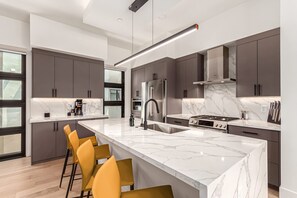 A modern kitchen with a marble island, stainless steel appliances, and yellow bar stools. - Papago Lux Townhouse 4level Oasis w Rooftop Lounge (Scottsdale)