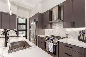 A modern kitchen with dark cabinets, a stainless steel range, and a marble countertop. - Papago Lux Townhouse 4level Oasis w Rooftop Lounge (Scottsdale)