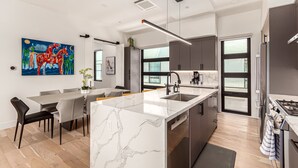 A modern kitchen with a marble island, stainless steel appliances, and a dining area with a large painting. - Papago Lux Townhouse 4level Oasis w Rooftop Lounge (Scottsdale)