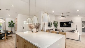 Una cocina moderna con una isla de mármol, luces colgantes y un comedor con mesa y sillas de madera.