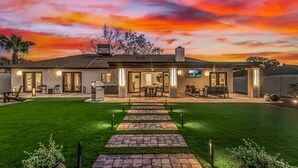 Una casa moderna con un camino de entrada pavimentado que conduce a un patio, mobiliario exterior y un césped bien cuidado.