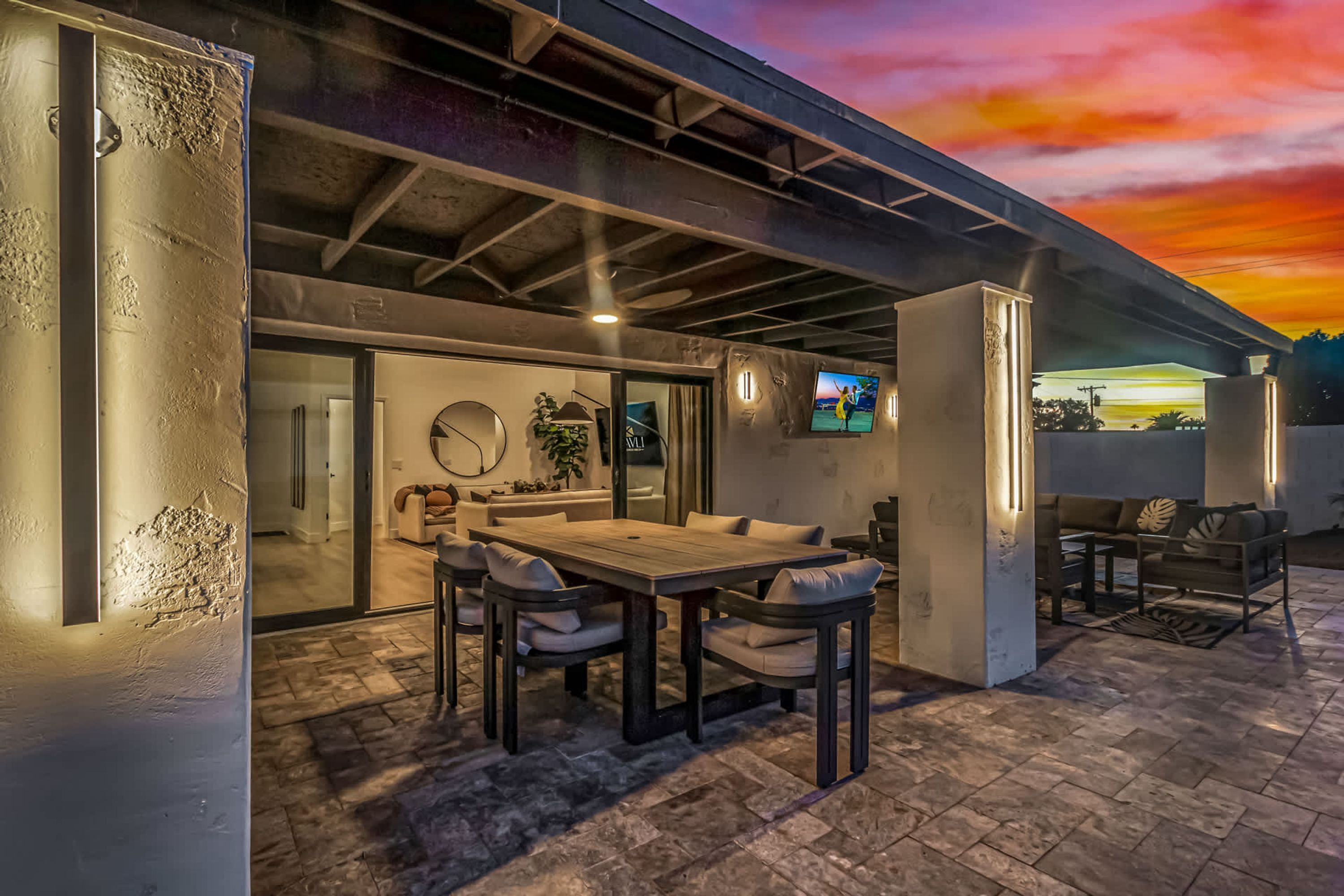 Un espacio al aire libre con un patio, una mesa y sillas de madera, un sofá y una pantalla de televisión.